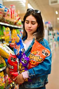 A young woman browsing snacks in a Mexican supermarket, holding an assortment of chips.